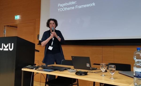 Sigrid Gramlinger steht vor einer Präsentationsleinwand zum Thema Barrierefreiheit mit Joomla mit einem Mikrofon in der Hand.